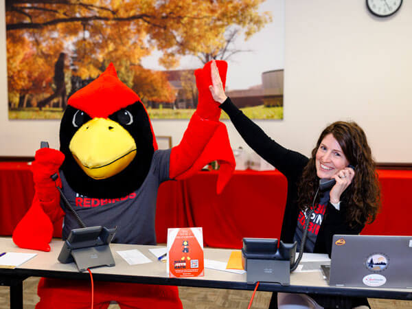 Reggie Redbird and a staff member high-five while answering phones for the Birds Give Back fundraising event.